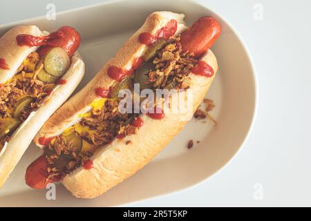 Klassischer Hot Dog mit Senf, Ketchup, Gurken und gebratenen Zwiebeln, Draufsicht, weißer Hintergrund, Fast-Food-Konzept. Stockfoto