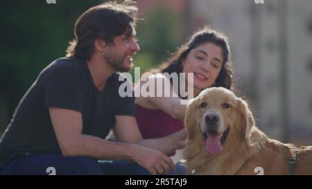 Glückliches Paar, das mit seinem Hund draußen im Stadtpark ein Wochenende verbracht hat. Ehrlicher Mann und ehrliche Frau und ihr Golden Retriever Pet. Millennial Lifestyle Stockfoto