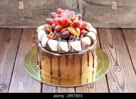 Herbstkuchen aus Schokolade, dekoriert mit Trauben, Walnüssen, Schokoladentrüffeln und Marshmallow. Rustikales Backgrond, komfortables Essen Stockfoto