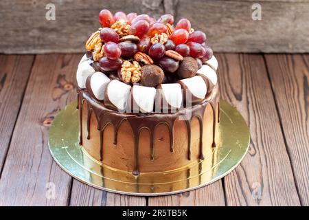 Herbstkuchen aus Schokolade, dekoriert mit Trauben, Walnüssen, Schokoladentrüffeln und Marshmallow. Rustikales Backgrond, komfortables Essen Stockfoto