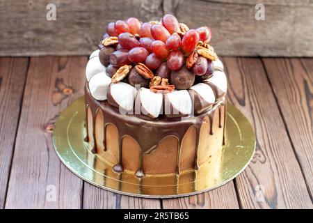 Herbstkuchen aus Schokolade, dekoriert mit Trauben, Walnüssen, Schokoladentrüffeln und Marshmallow. Rustikales Backgrond, komfortables Essen Stockfoto