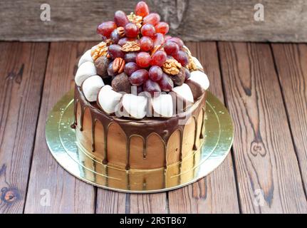 Herbstkuchen aus Schokolade, dekoriert mit Trauben, Walnüssen, Schokoladentrüffeln und Marshmallow. Rustikales Backgrond, komfortables Essen Stockfoto