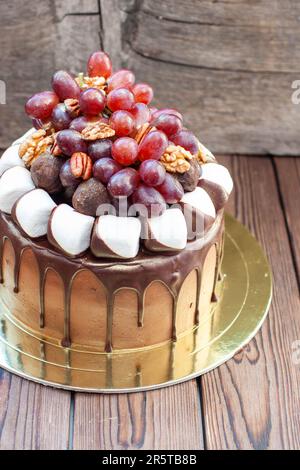 Herbstkuchen aus Schokolade, dekoriert mit Trauben, Walnüssen, Schokoladentrüffeln und Marshmallow. Rustikales Backgrond, komfortables Essen Stockfoto