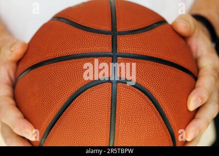 Roter Basketball in den Händen einer Nahaufnahme auf weißem Hintergrund Stockfoto