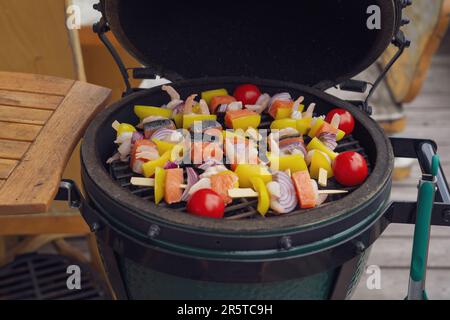 Rohe Grillgarnelen Spieße mit Lachs und Gemüse zum Grillen auf einem Holzkohlegrill auf dem Balkon an einem Sommertag Stockfoto