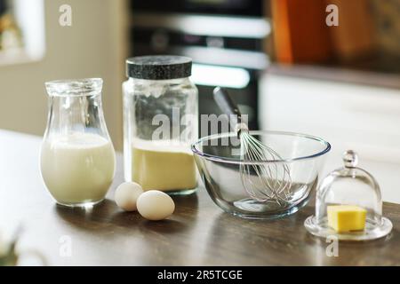 Butter in einem Butterteller und Eier, Milch und Mehl auf einem Tisch Stockfoto