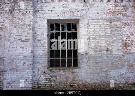 Seitlicher Blick auf ein traditionelles Ziegelgebäude mit einem altmodischen verschließbaren Fenster, durch das die Sonnenstrahlen hindurchströmen Stockfoto