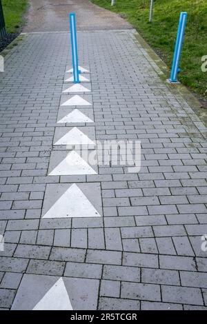 Eine Straße mit einem gelben Pfeil auf dem Boden, der mit weißen und blauen Markierungen markiert ist und die Richtung angibt, der die Fahrer folgen müssen Stockfoto