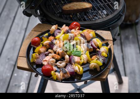 Fertig zum Essen - gegrillte Garnelen mit Lachs und Gemüse auf einem schwarzen Teller, von einem grill an einem Sommertag auf dem Balkon Stockfoto