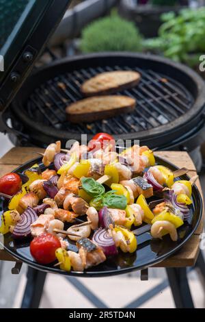 Fertig zum Essen - gegrillte Garnelen mit Lachs und Gemüse auf einem schwarzen Teller, von einem grill an einem Sommertag auf dem Balkon Stockfoto