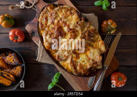 Lasagne mit geröstetem Kürbis, Käseplatte auf rustikalem Holztisch Stockfoto