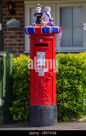 Sussex, Vereinigtes Königreich - April 30. 2023: Ein gestrickter Postfachaufsatz auf einem roten Postfach im Dorf Cowfold in West Sussex, Vereinigtes Königreich. Stockfoto