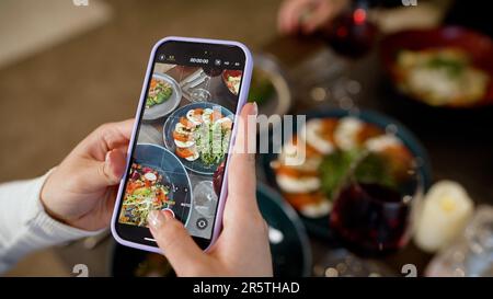 Die Hände einer Nahaufnahme nehmen Essen per Telefon. Nahaufnahme der Hände einer Frau mit einem Smartphone, um ein Foto von Essen zu machen. Weibliche Hände machen ein Foto auf einem Stockfoto