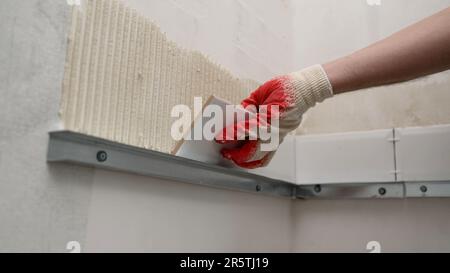 Industrielle Nahaufnahme einer Arbeiterhand, die Zementkleber zum Verlegen von Keramikfliesen aufträgt. Befestigen von Fliesen an der Wand. Fliesen an die Wand legen. Stockfoto