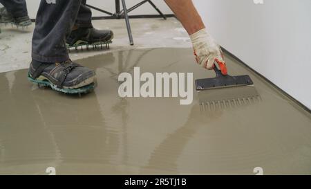 Der Prozess des Ausgleichs von Zement mit einem Spachtel, der Meister hält ein Werkzeug in der Hand und führt es durch den Zement. Verteilen Sie den Zementboden mit einem Stockfoto