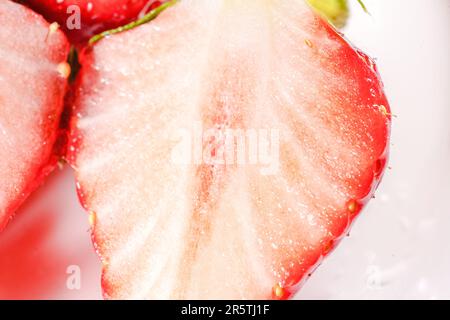 Eine farbenfrohe Ausstellung reifer Erdbeeren, in zwei Hälften geschnitten, präsentiert auf einem weißen Teller Stockfoto