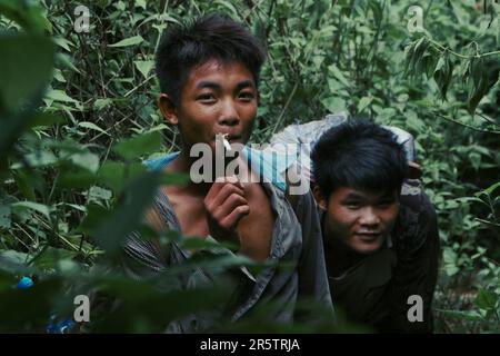 Zwei junge Jungs, Freunde, die im Moment leben, eine Zigarette genießen, während sie vom wilden Dschungel umschlossen und eingerahmt werden. Stockfoto