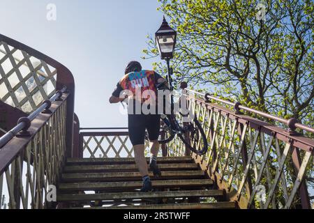 27.05.2023 Kirkby Stephen, Cumbria, Vereinigtes Königreich. Radfahrer, der sein Fahrrad über die Brücke am Bahnhof Kirkby Stephen schleppt Stockfoto