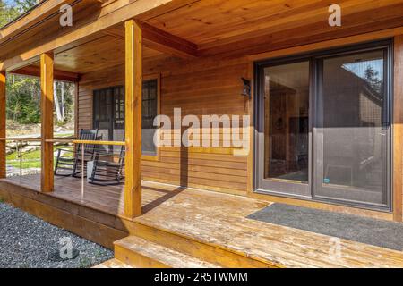Eine gemütliche Veranda mit rustikalen Holzmöbeln auf einem weißen Holzhaus mit großen Fenstern Stockfoto
