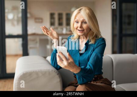 Aufgeregte Erwachsene Frau, die auf den Smartphone-Bildschirm schaut, emotional auf gute Nachrichten reagiert, während sie zu Hause auf der Couch sitzt Stockfoto
