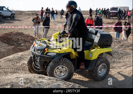 Ein fetter, schwarz gekleideter Mann, der auf einem gelben Suzuki Kingquad Quad durch das Gelände fährt Stockfoto