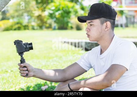 Nahaufnahme eines jungen Latinos, der ein tragbares Video aufnahm, an einem Sommertag, der auf dem Gras saß Stockfoto