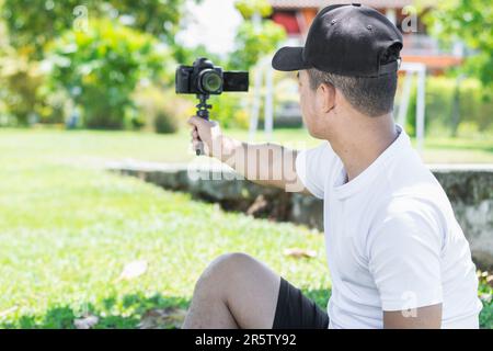 Dynamische Aufnahme von hinten eines jungen Latino-Influencer, der fesselnde Aufnahmen mit einer Handkamera aufnimmt und so eine einzigartige Perspektive auf seine Kreation bietet Stockfoto