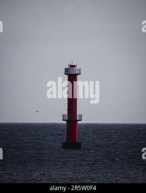 Ein majestätischer Leuchtturm steht hoch am Rand eines riesigen Wasserkörpers, dessen weißer Turm von der untergehenden Sonne beleuchtet wird Stockfoto