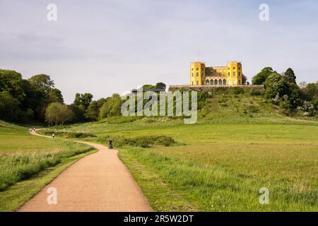 Die Menschen gehen und joggen auf dem Frome Greenway Pfad durch Stoke Park in Bristol, mit dem Wahrzeichen „Yellow Castle“ Dower House auf dem Hügel dahinter. Stockfoto