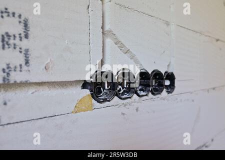 Schwarze Kunststoffkästen mit runden Löchern für Kabel und Steckdosen, die im neuen Hausgebäude installiert sind Leerwand, Nahaufnahme Stockfoto