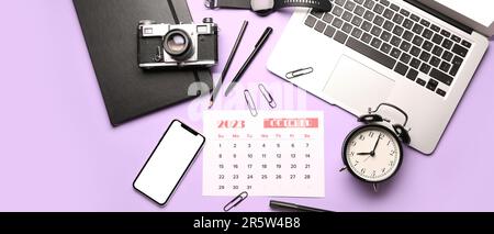 Kalender für Oktober 2023, Wecker, Laptop, Handy, Fotokamera und Bürobedarf auf lila Hintergrund Stockfoto