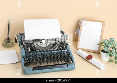 Vintage-Schreibmaschine, leerer Rahmen, Brille und Schriftrolle mit Wachssiegelstempel auf beigefarbenem Hintergrund Stockfoto