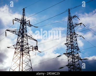 Hochspannungssäulen auf blauem Himmelshintergrund mit Wolken. Metallgelagerte Hochspannungsleitung. High-Tech-Stromleitungen Stockfoto