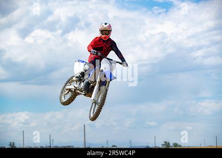 Ein weißer Mann, der mitten in der Luft einen Stunt-Sprung auf einem Dirt-Bike vorführt Stockfoto