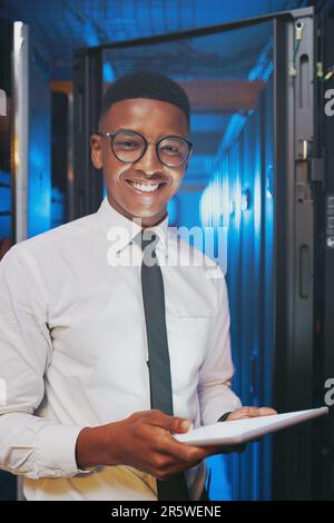 Sie freuen sich, dass Ihre Daten sicher sind. Ein junger IT-Spezialist, der allein im Serverraum steht und ein digitales Tablet verwendet. Stockfoto