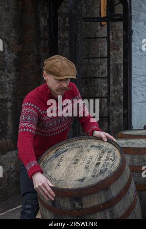 Arbeiter, der in der Whisky-Destillerie, Springbank, Schottland, Whisky-Fass rollt. Stockfoto