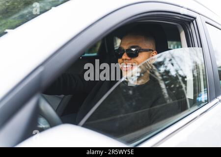 Ein hübscher junger Schwarzer, der Auto fährt, mit einem halboffenen Glasfenster und Seitenansicht. Hochwertiges Foto Stockfoto