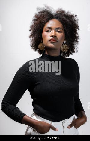 Eine afroamerikanische Frau nimmt eine selbstbewusste Pose vor einem soliden weißen Hintergrund ein Stockfoto