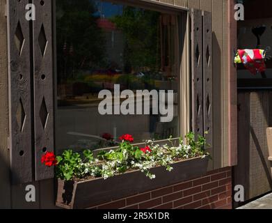 Traditionelle Fensterbox mit Geranien unter einem großen Fenster, das die lokale Szene in Sugarcreek, Ohio, widerspiegelt Stockfoto