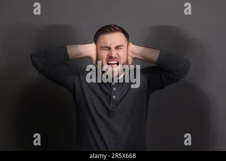 Er leidet an Halluzinationen. Ein Mann schreit und schließt die Ohren, um keine Schatten um ihn herum zu hören Stockfoto