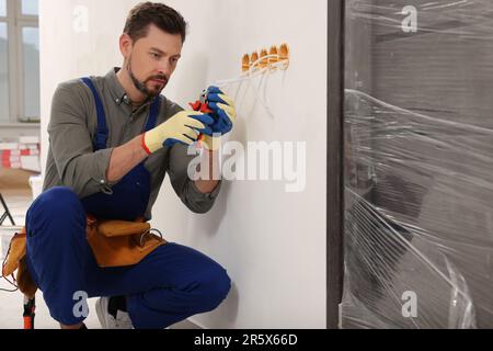 Elektriker in Uniform mit Zangen, die Steckdosen in Innenräumen reparieren Stockfoto