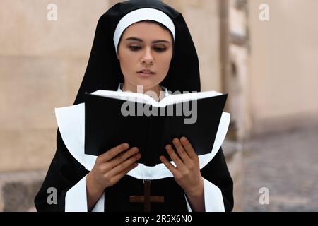 Junge Nonne liest Bibel in der Nähe von Gebäuden im Freien Stockfoto