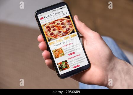 Lebensmittellieferservice. Mann wählt Gericht aus der Speisekarte vor Ort mit Smartphone drinnen, Nahaufnahme Stockfoto