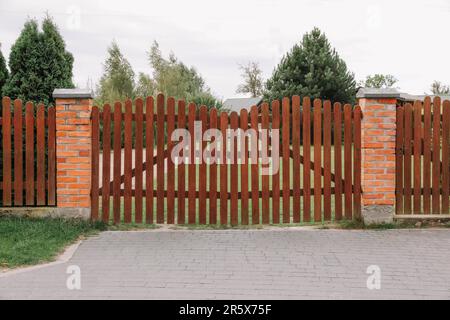 Hölzerne braune Tore in der Nähe von wunderschönen Bäumen und Rasen im Freien Stockfoto