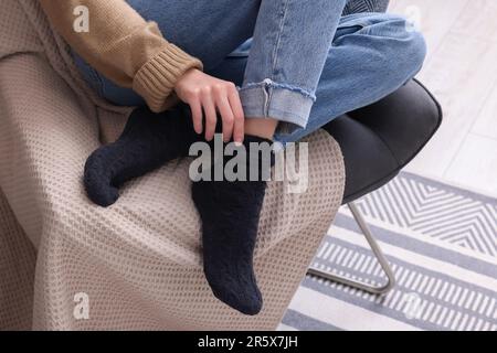 Eine Frau in warmen Socken, die zu Hause auf einem Sessel sitzt, schließt Stockfoto