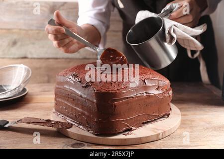 Frau, die Schokoladencreme in hausgemachten Schwammkuchen am Holztisch schüttet, Nahaufnahme Stockfoto