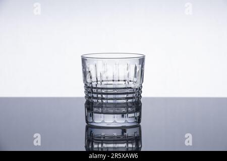 Whiskey-Kristallglas auf einer reflektierenden Oberfläche. Isoliertes Objekt. Dramatischer moderner Hintergrund. Modernes Design. Stockfoto
