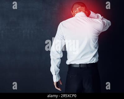 Ich fühle die Spannung eines stressigen Tages. Studioaufnahme eines jungen Geschäftsmannes mit Nackenschmerzen, rot leuchtend. Stockfoto