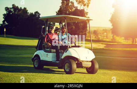 Ab zum ersten Abschlag. Zwei Golfer, die in einem Wagen auf einem Golfplatz reiten. Stockfoto