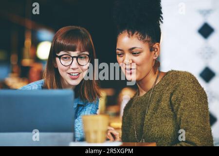 Suchen wir nach weiteren lustigen Clips, die Sie sich ansehen können. Zwei junge Freunde, die sich in einem Café auf einem digitalen Tablet etwas ansehen. Stockfoto